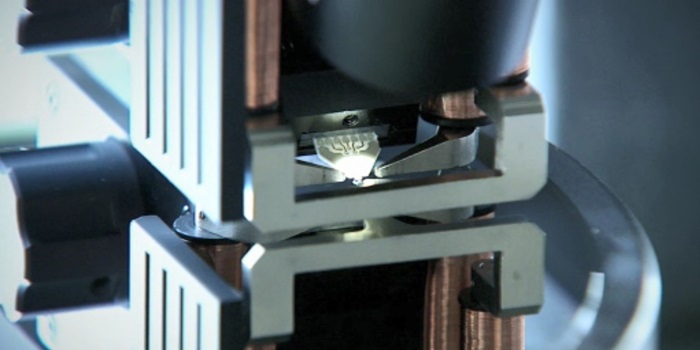 Målehoved og dets spejlbillede under måling af tyndfilmsegenskaberne på en wafer. Mikroproben er monteret og oplyst i midten af målehovedet om-givet af polsko for at kunne styre magnetfeltet.