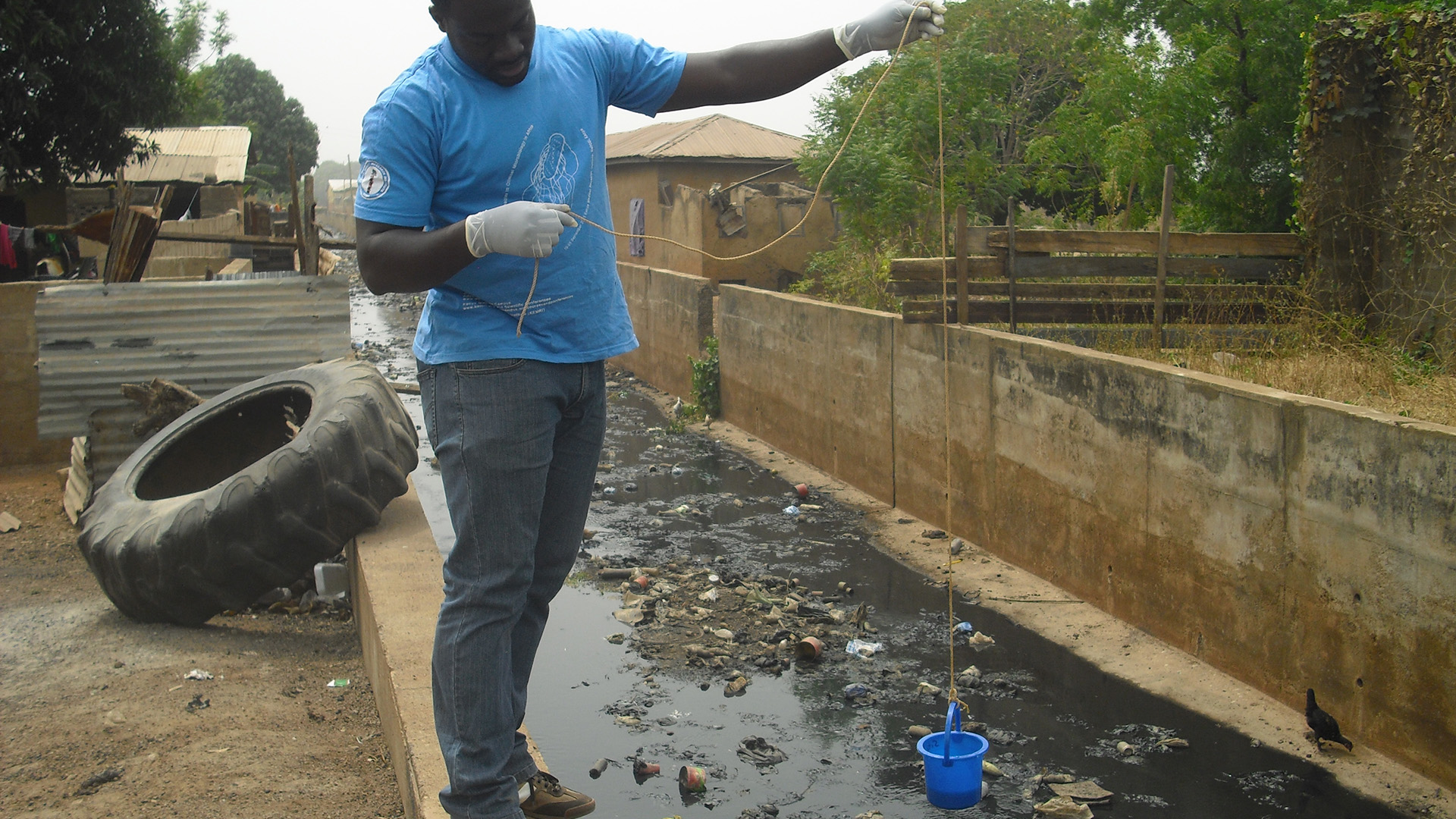 Mand tager spildevandsprøve fra åbent kloaksystem