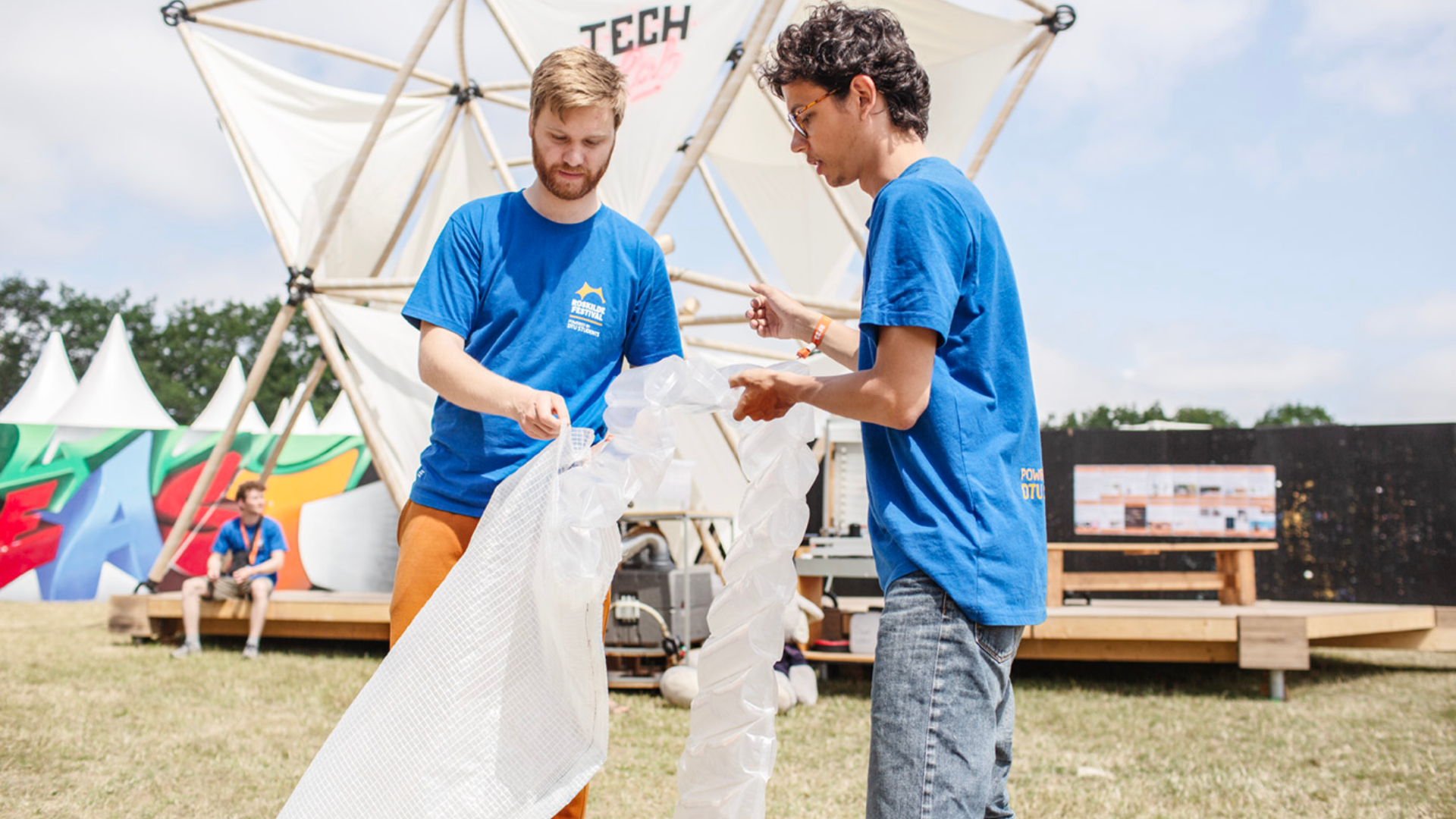 To DTU-studerende i blå t-shirts fylder oppustelig plastik i en plastikmadras på Roskilde Festival.