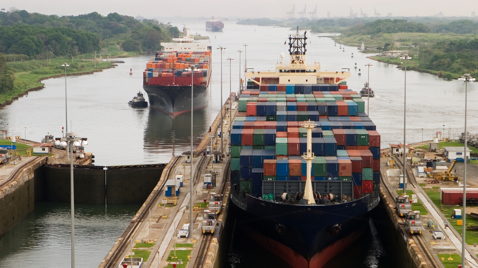 Et stort containerskib fuldt lastet med containere holder i Panamakanalen, mens flere andre containerskibe venter i baggrunden.