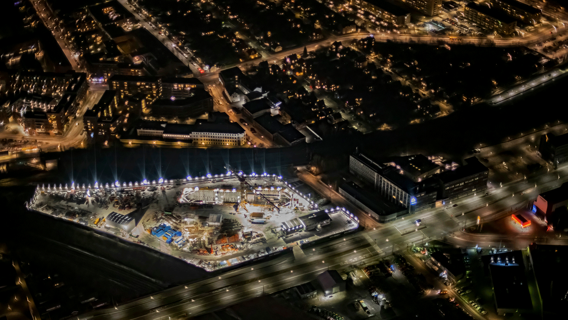 En byggeplads lyser op med dens mange projektorer i en by om natten.