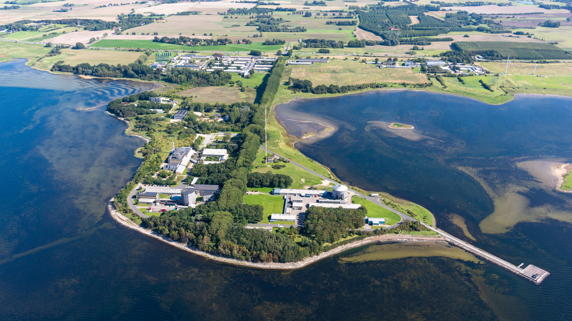 Luftfoto af Risø Campus med halvøen i forgrunden og grønne marker i baggrunden.