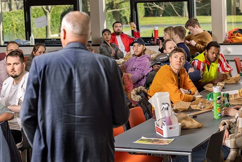 Photo by Mikal Schlosser. Featured is President Anders Bjarklev talking to a group of new students sitting in a canteen. 