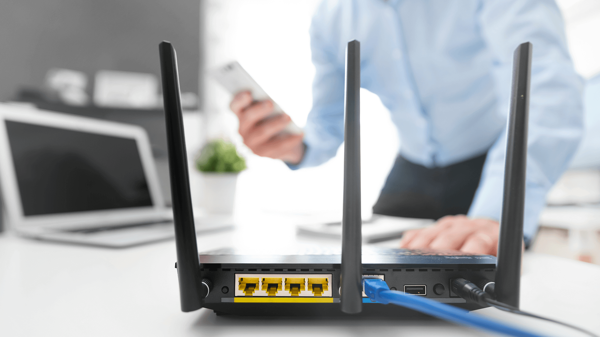 Router står på et bord, en mand står i baggrunden med en mobiltelefon i hånden.