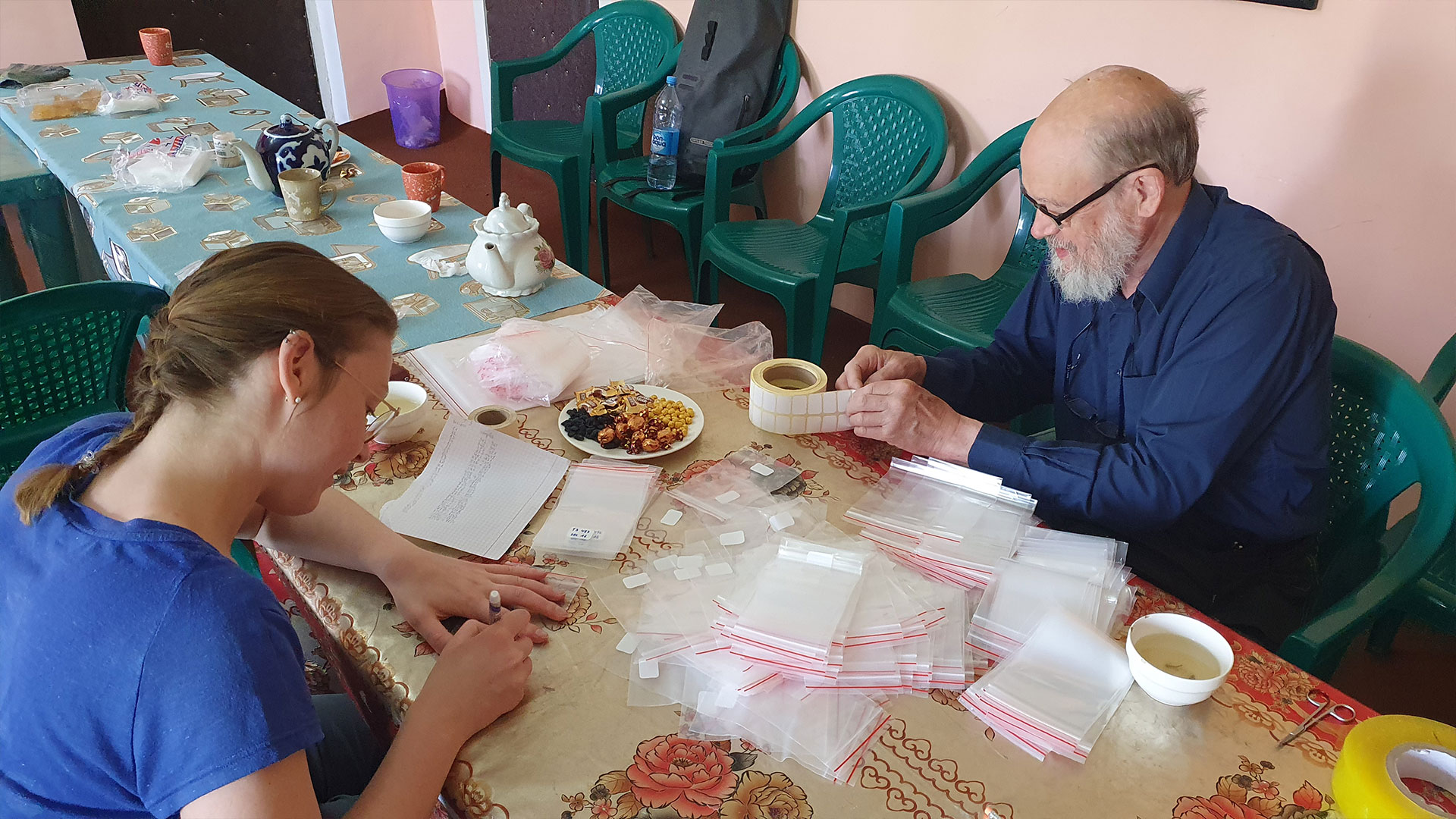 A woman and a man sitting at a table putting labels on small plastic bags. Photo: Miriam Meister
