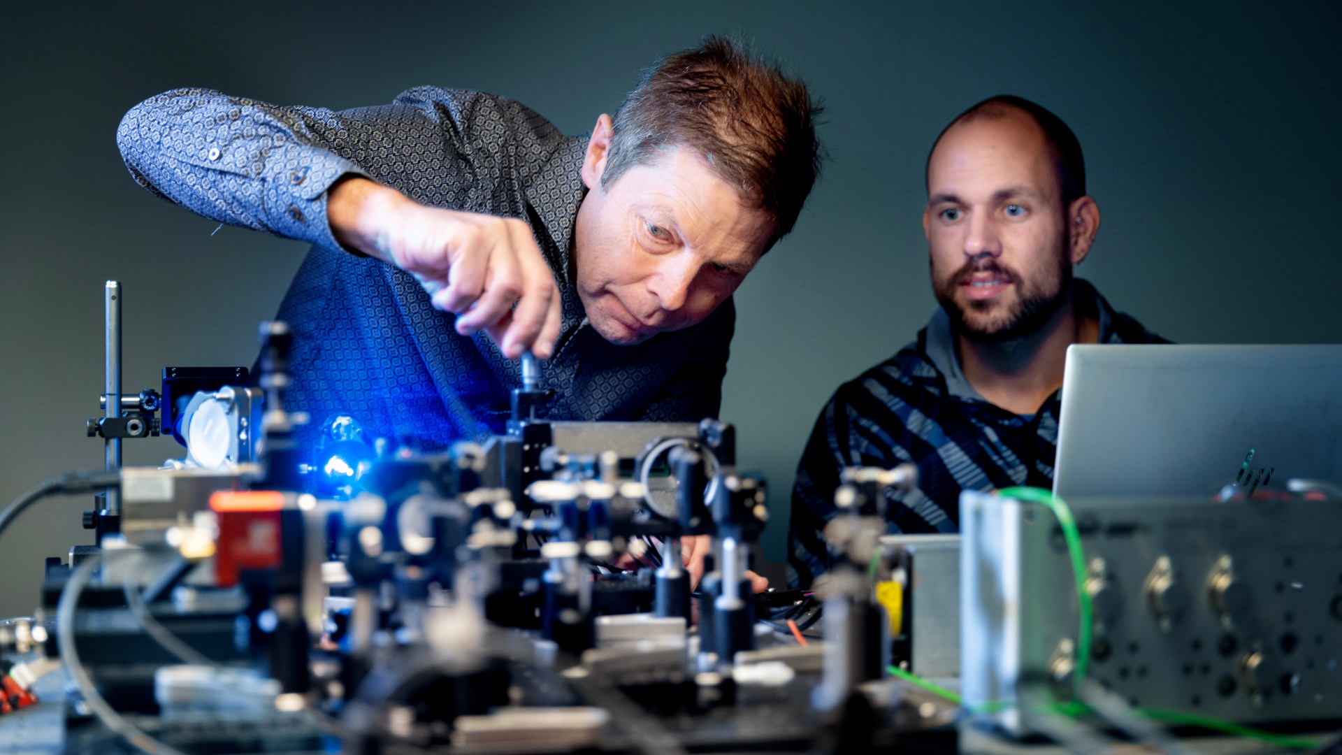 Christian Pedersen står bøjet ind over et laserapparat og skruer på en knap, mens Joaquim Santos ser på.