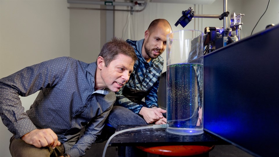 Christian Pedersen studerer en gennemsigtig, cylinderformet tank fyldt med vand, hvor en blå laser skyder ned på nogle mikroalger.