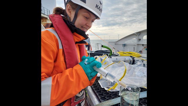 Woman wearing safety equipment onboard a boat is collecting water samples. Photo: Tim Wilms