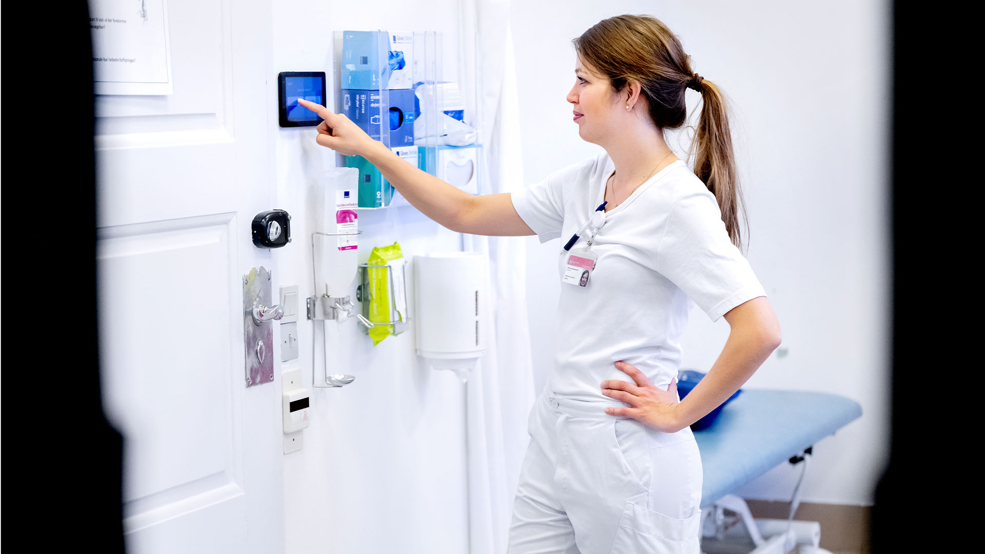 A nurse is standing by a wall-mounted digital display. Photo: Bax Lindhardt