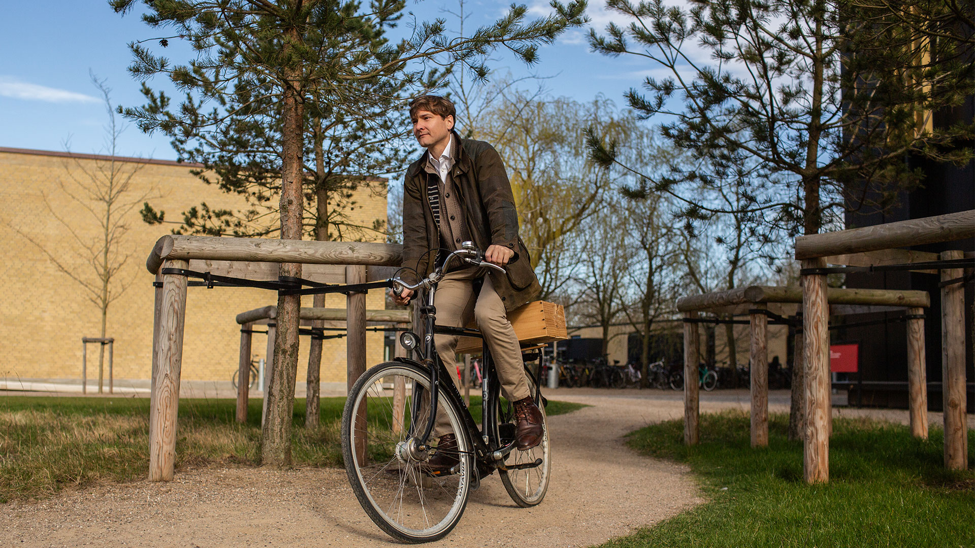 Man bicycles through an area with some vegetation and buildings. Photo: Ditte Valente