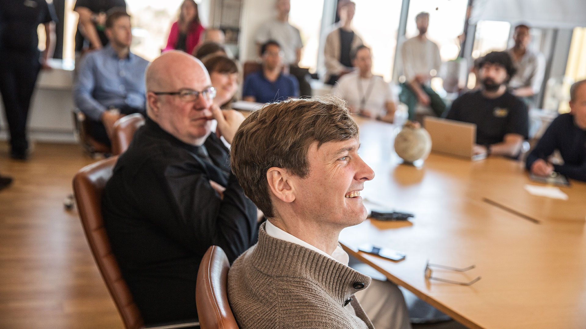 A man with a broad smile sits amongst a group of people around a table. Photo: Ditte Valente